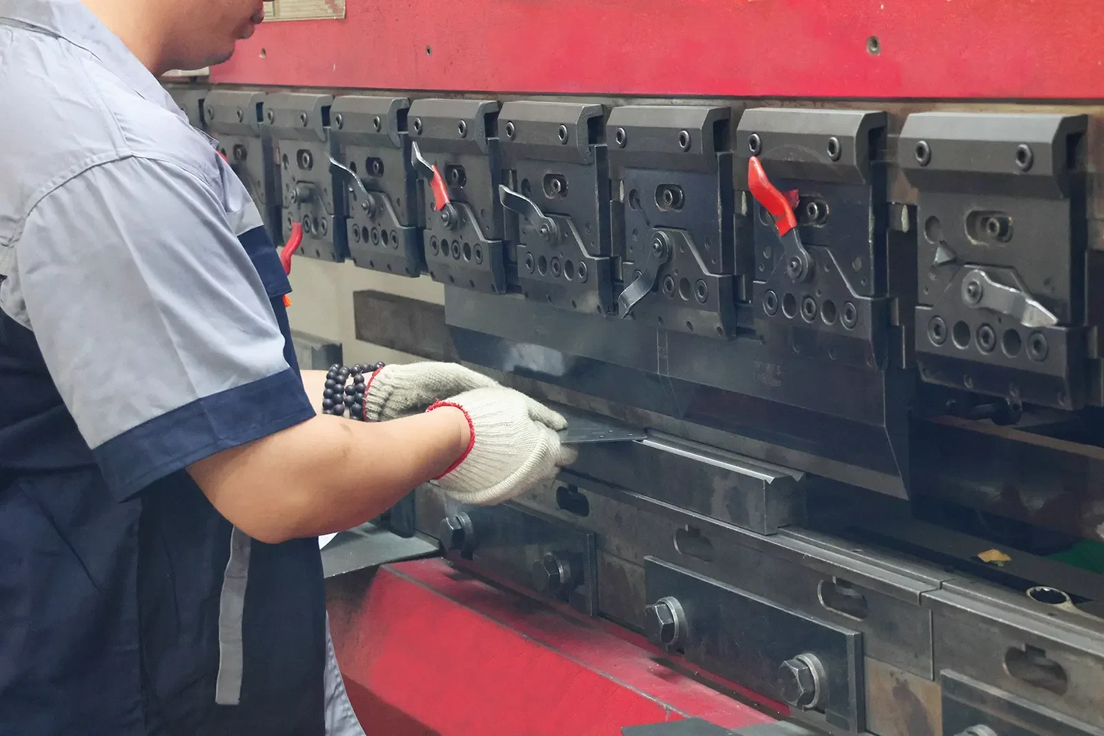 Worker bending sheet metal with CNC hydraulic press brake machine in metal fabrication workshop, custom sheet metal bending processing