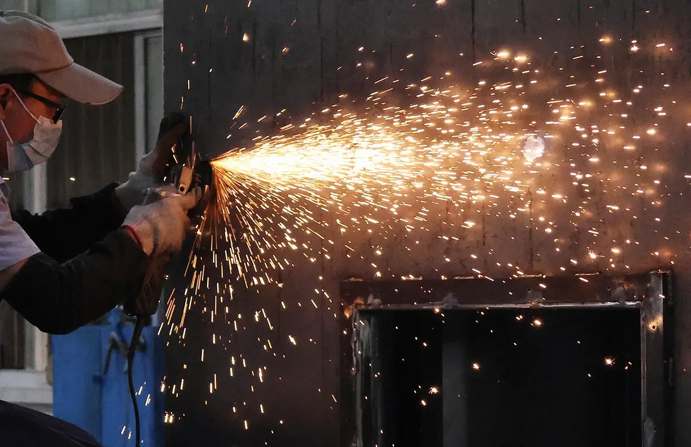 Worker carrying out surface grinding finishing on industrial sheet metal equipment frames
