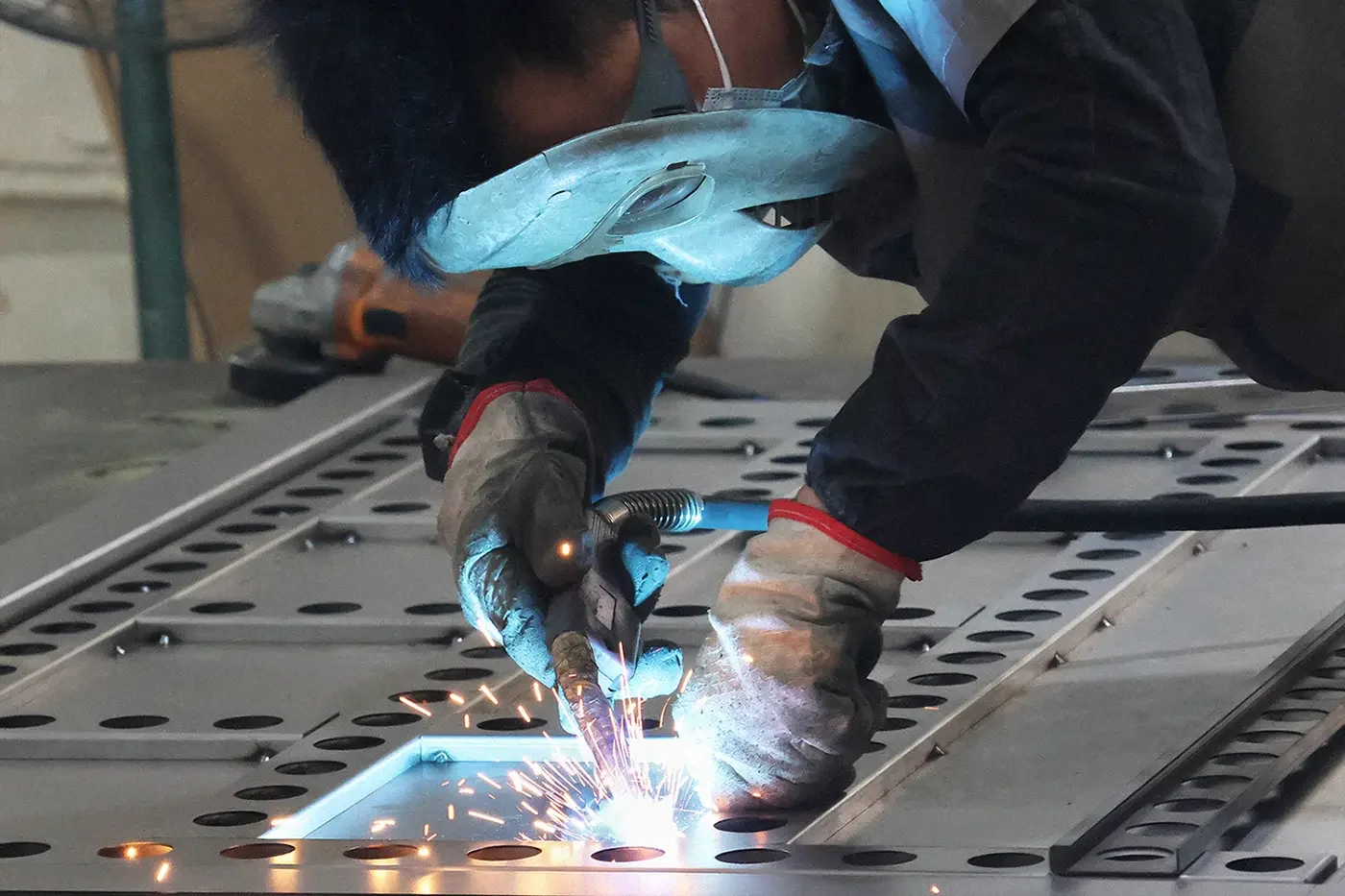 Skilled worker welding steel sheet metal during custom EV charger enclosure fabrication