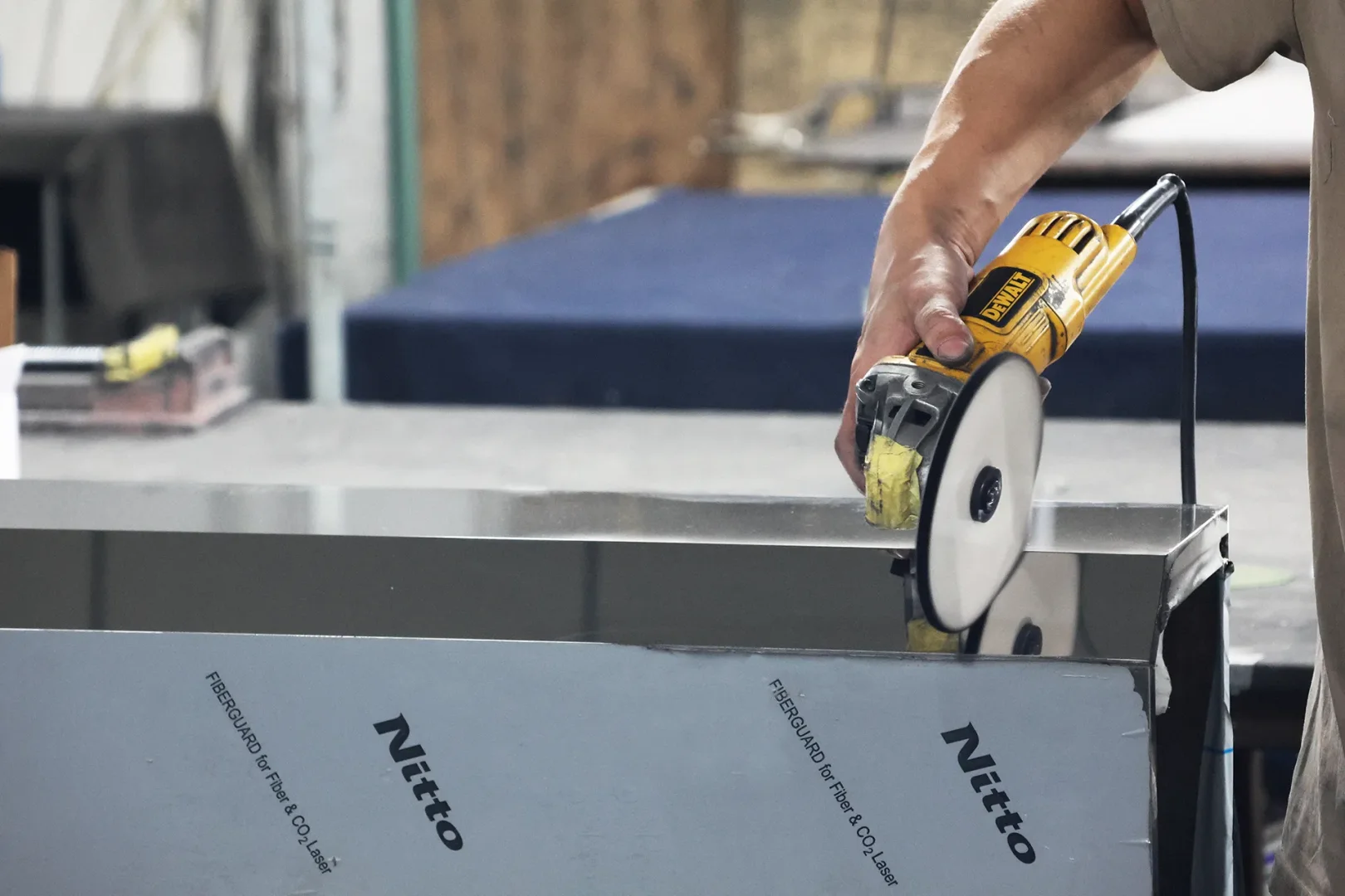 Worker using angle grinder to deburr and polish sheet metal edge during custom EV charger enclosure fabrication